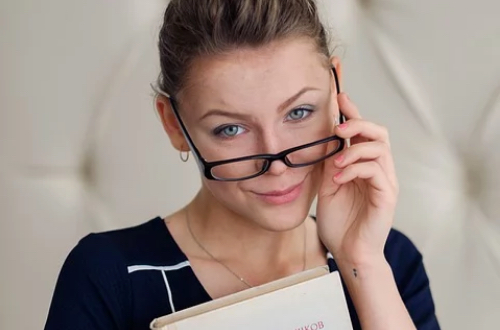 A woman with glasses is holding a book in her hand.