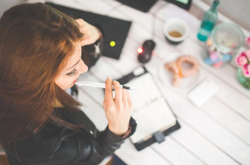 A woman sitting at the desk with a pen in her hand. There's a notebook on the desk.